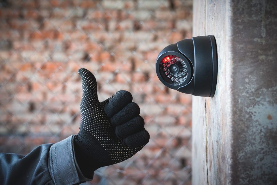 main de technicien montrant un pouce en l'air à côté d'une camera de vidéosurveillance installée sur un mur